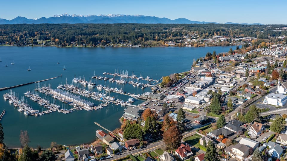 A marina with boats, a town with houses, and mountains in the background.