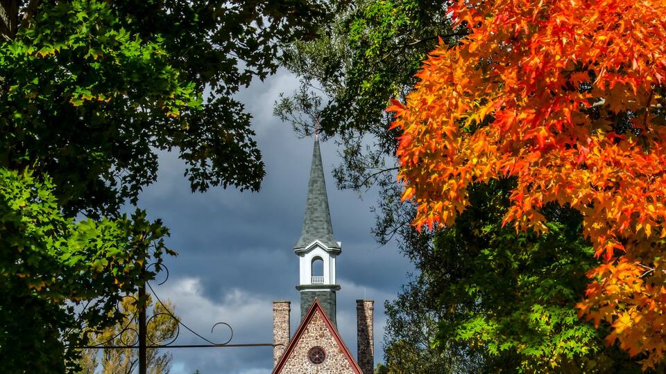 A church with a steeple, surrounded by autumn foliage and a pathway leading to it.