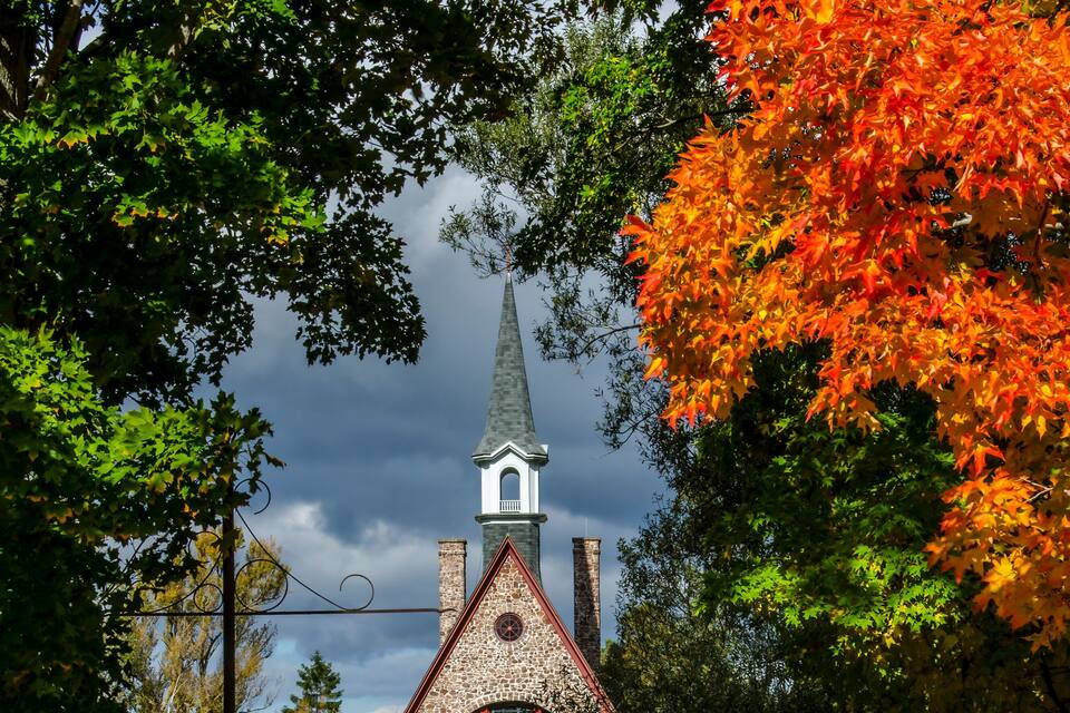 A church with a steeple, surrounded by autumn foliage and a pathway leading to it.