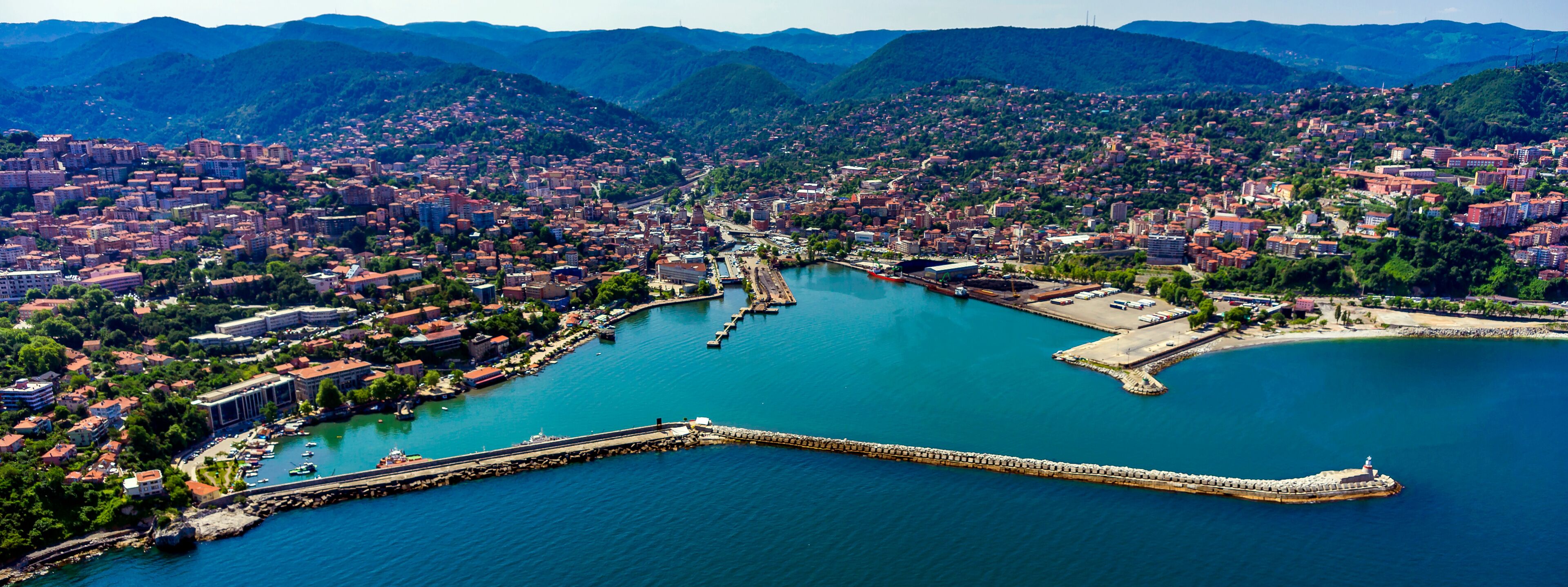 A coastal city with a harbor, a lighthouse, and surrounding mountains.