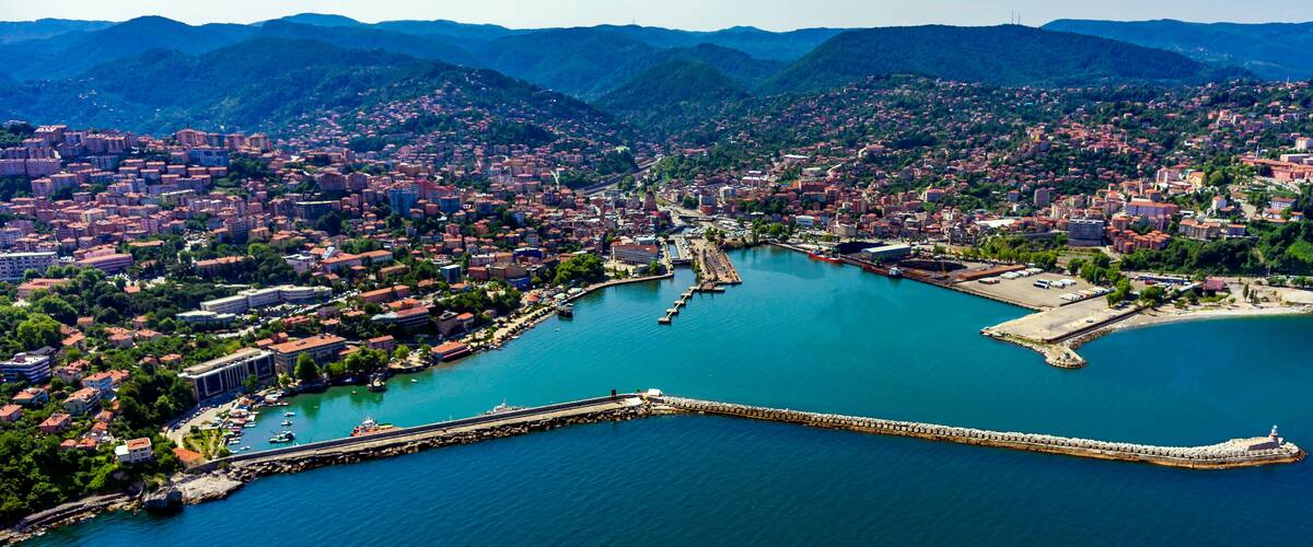 A coastal city with a harbor, a lighthouse, and surrounding mountains.