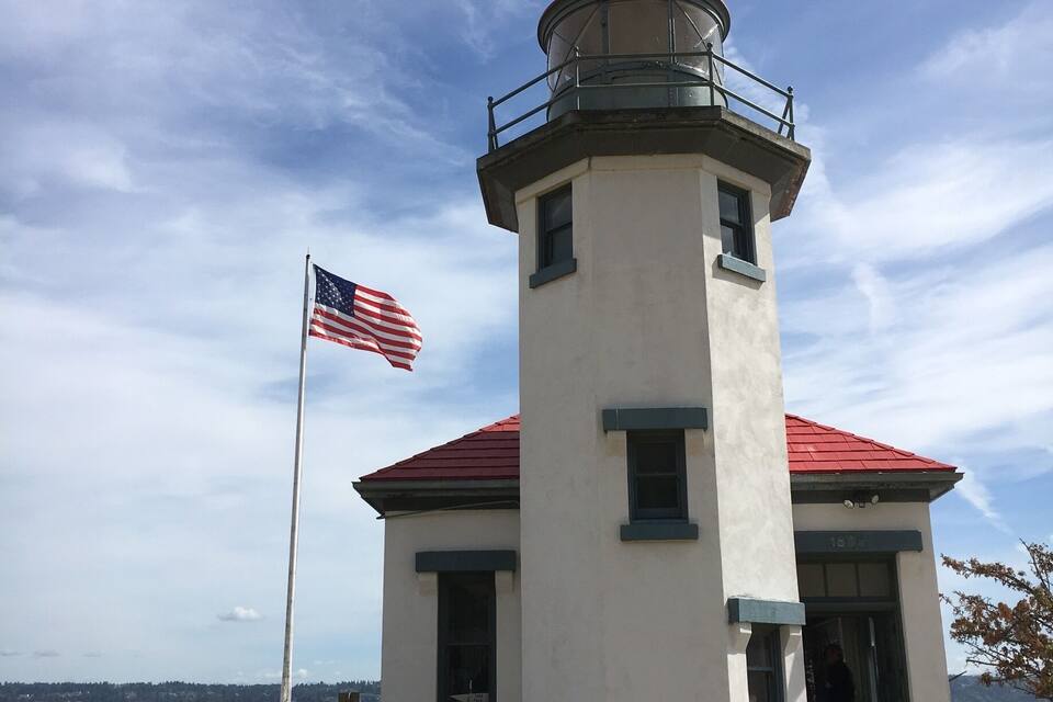 Un faro con techo rojo y un asta con la bandera estadounidense.