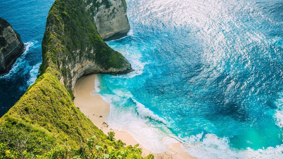 A coastal landscape with a beach, rocky cliffs, and turquoise waters.