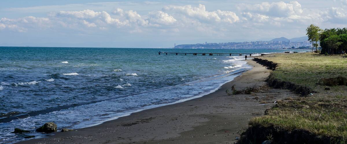 Une plage avec des vagues, une jetée et, au loin, la silhouette d’une ville.