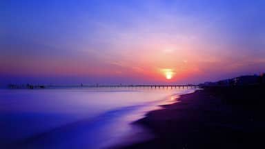 A sunset over a calm beach with a pier extending into the water.