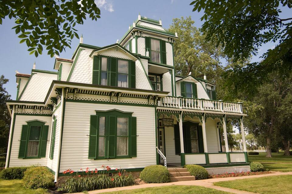 Une maison blanche avec des volets verts et une véranda.
