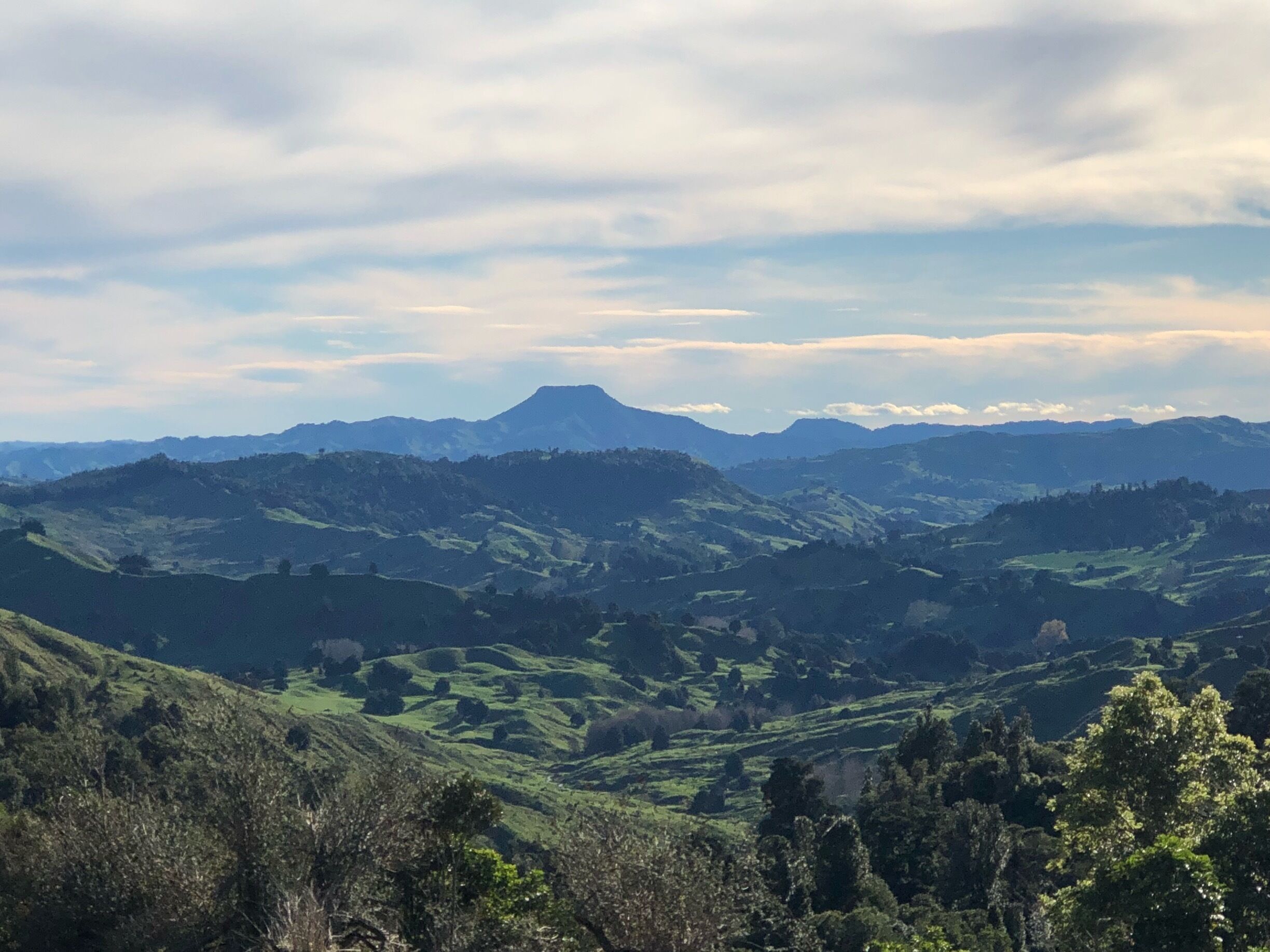 A mountainous landscape with rolling hills and a prominent mountain peak in the distance.