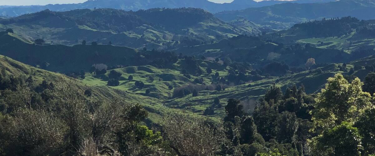 A mountainous landscape with rolling hills and a prominent mountain peak in the distance.
