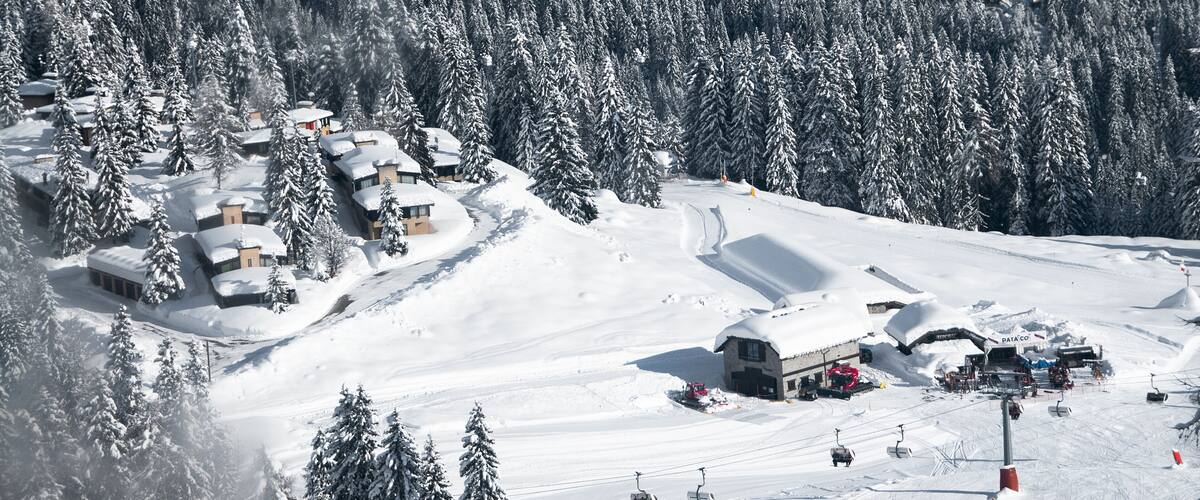 A snow-covered ski resort with cabins, ski lifts, and a forested mountain backdrop.