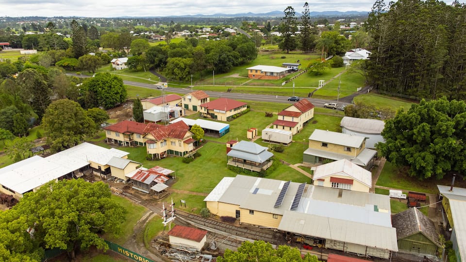 An aerial view of a small town with houses, a railway line, and surrounding greenery.