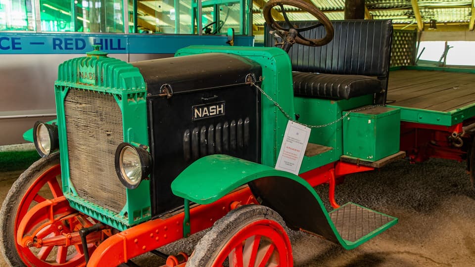 A vintage Nash car with green and red paint, a steering wheel, and a bench seat.