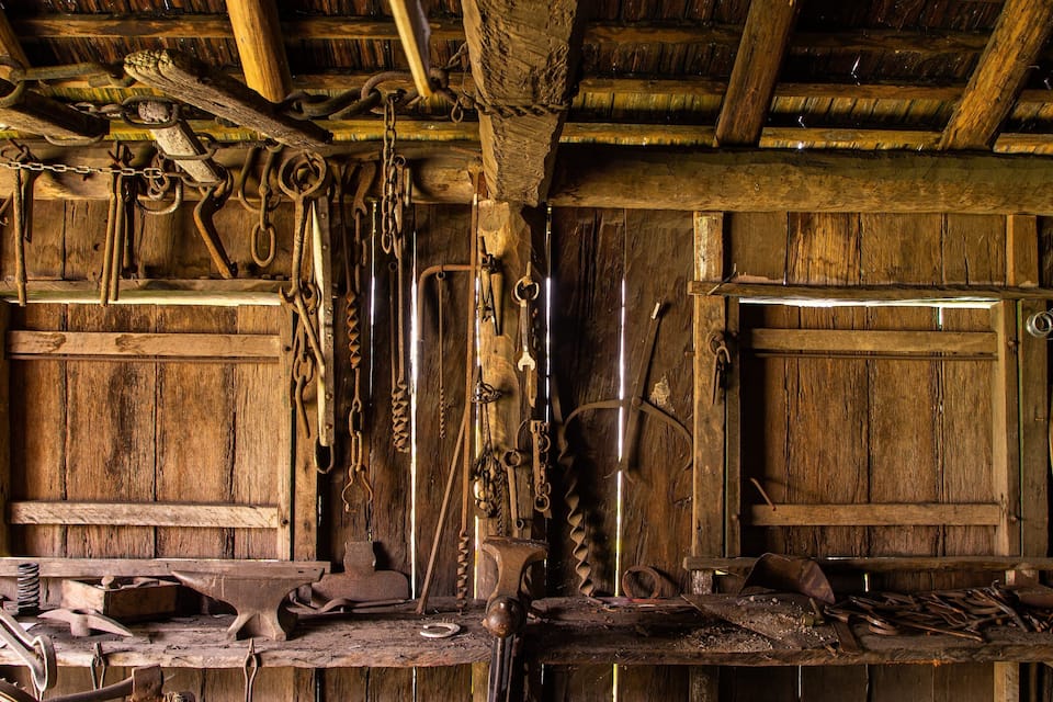 An old wooden forge with tools hanging on the walls and a workbench cluttered with metal objects.
