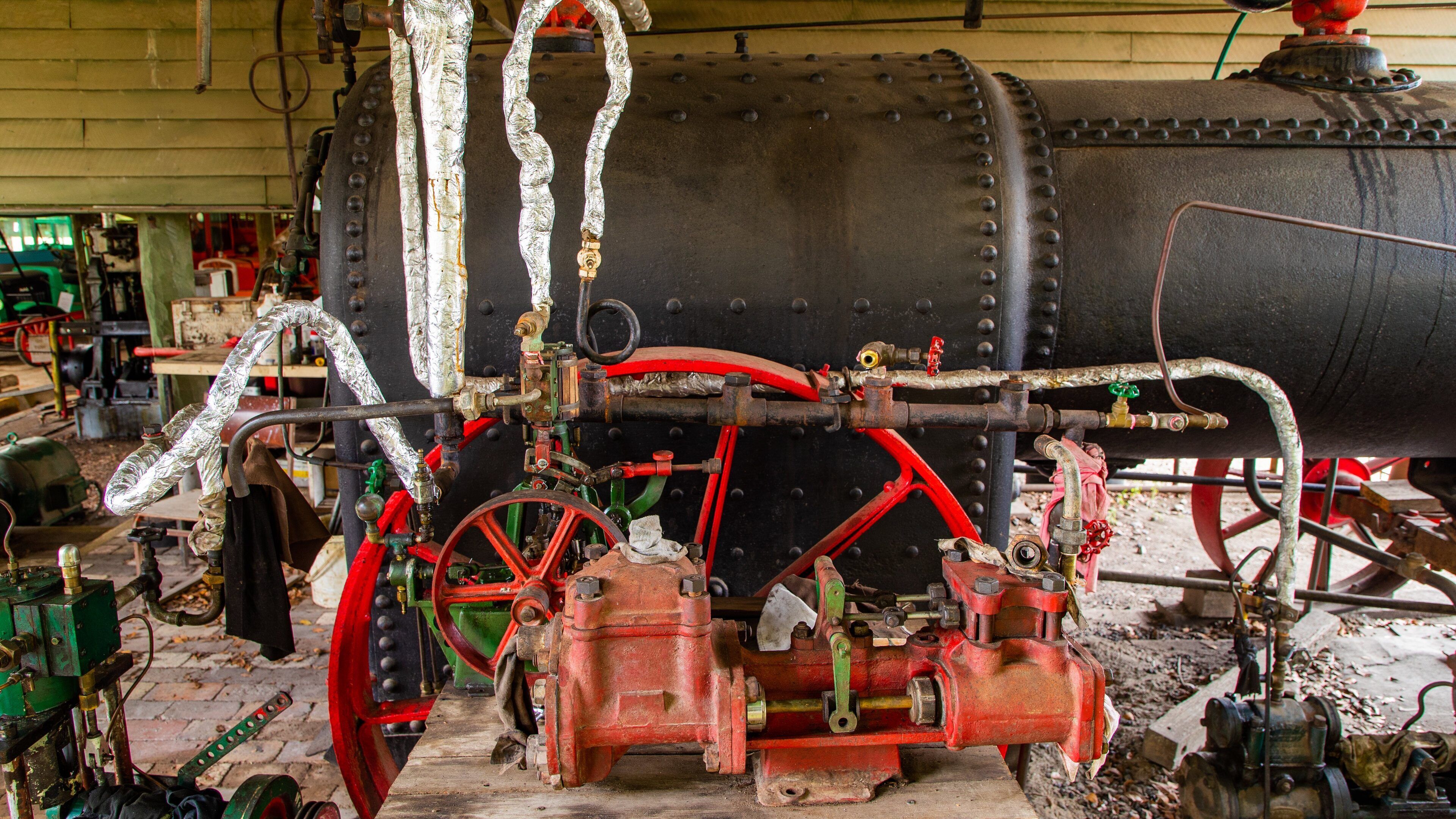 Uma grande caldeira industrial preta com tubulações vermelhas e verdes e rodas.