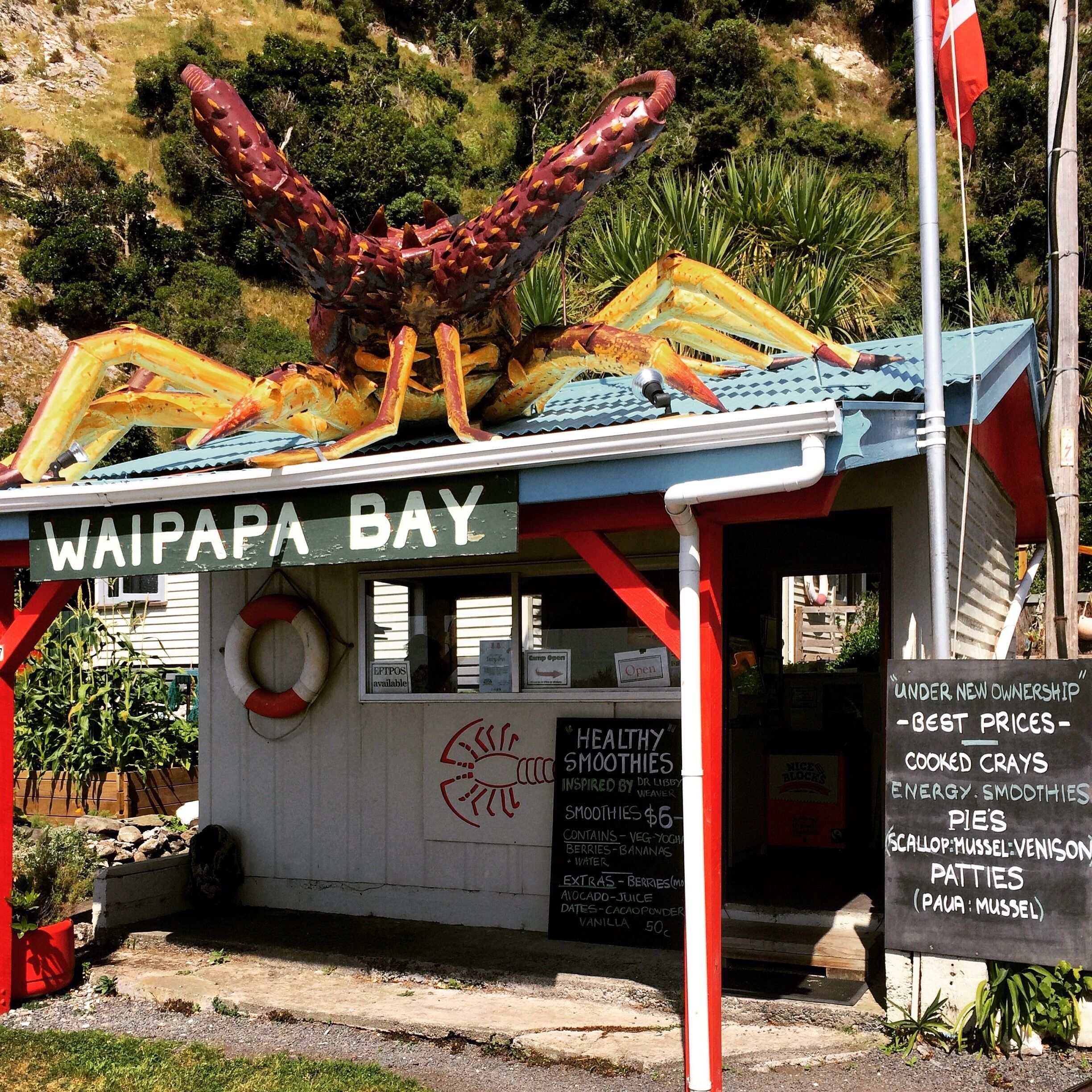 A small food stall named Waipapa Bay with a sign advertising healthy smoothies and cooked crays.