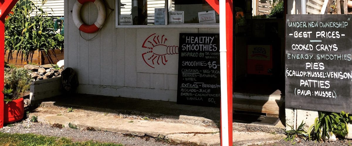 A small food stall named Waipapa Bay with a sign advertising healthy smoothies and cooked crays.