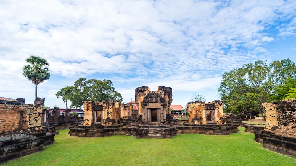 Ancient ruins with a central structure, surrounded by stone walls and lush greenery.