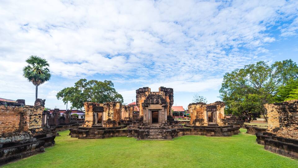 Ancient ruins with a central structure, surrounded by stone walls and lush greenery.