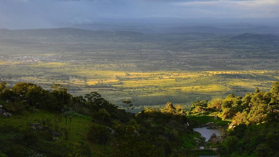 A panoramic view of a valley with a river, rolling hills, and scattered buildings.