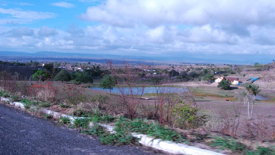 A rural landscape with a road, fields, a pond, and distant mountains.