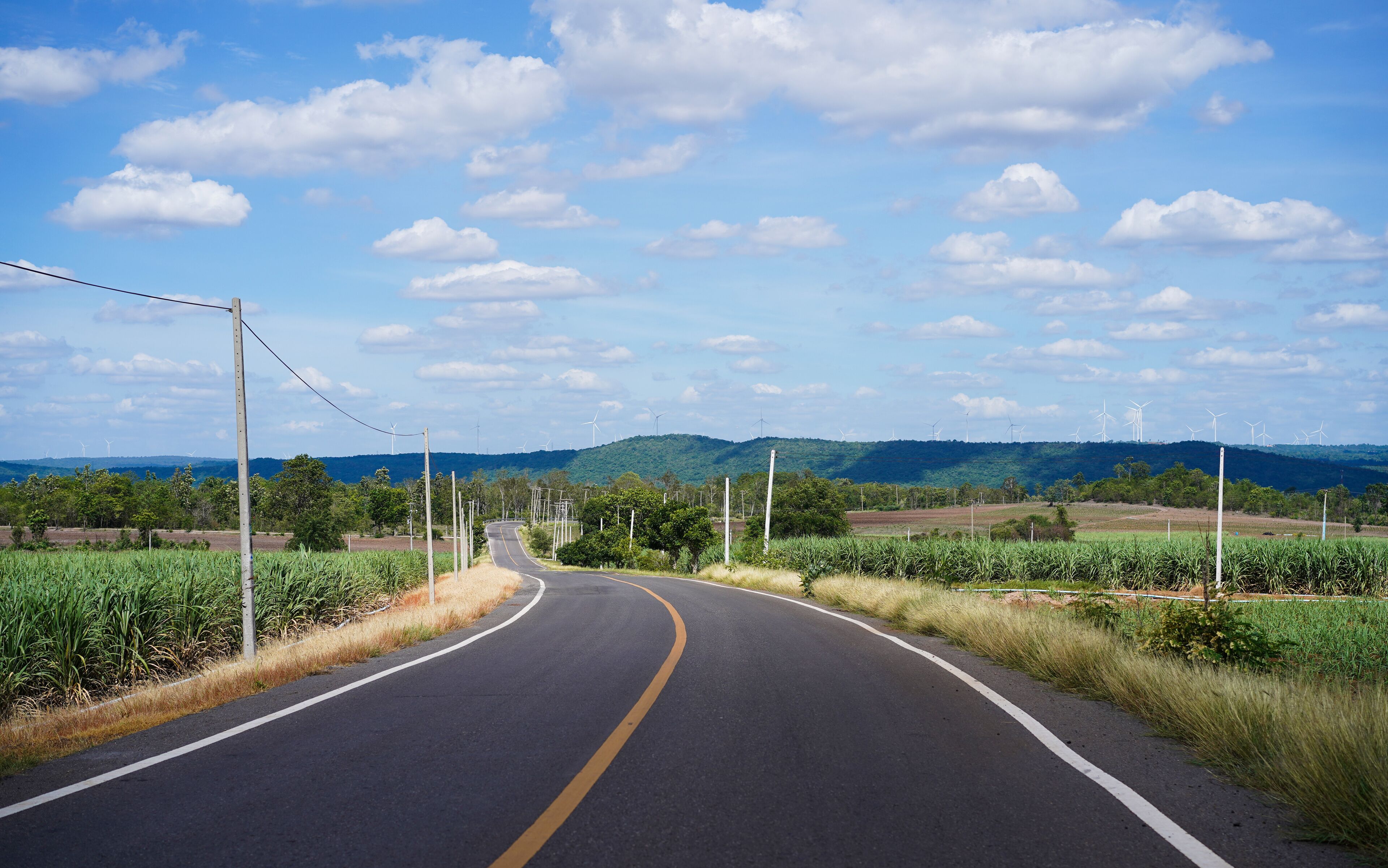A winding road with wind turbines in the distance and a clear blue sky.