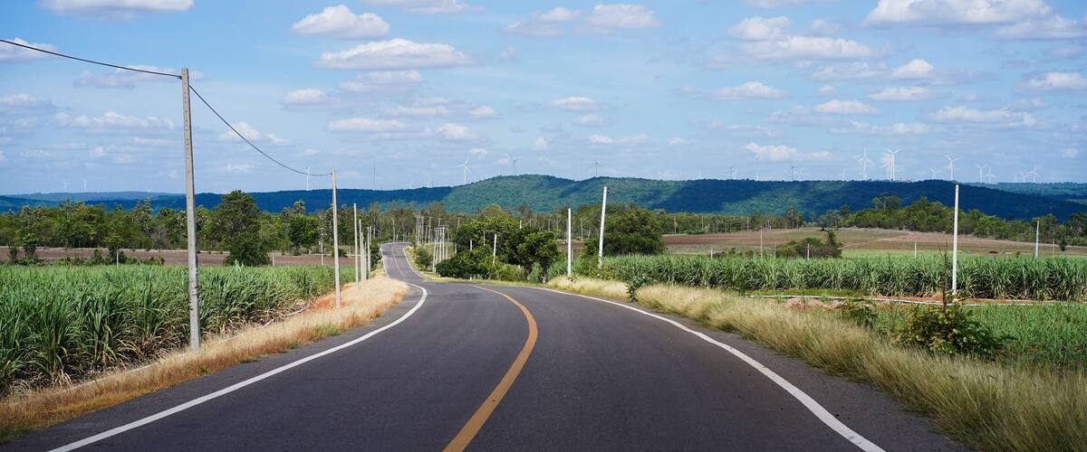 A winding road with wind turbines in the distance and a clear blue sky.