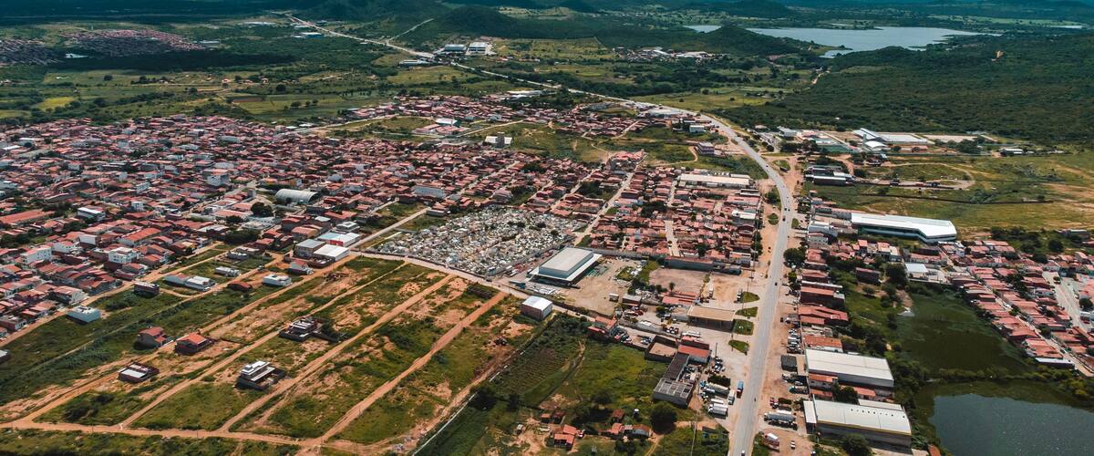 An aerial view of a town with red-roofed houses, a large industrial area, and surrounding green hills and a lake.