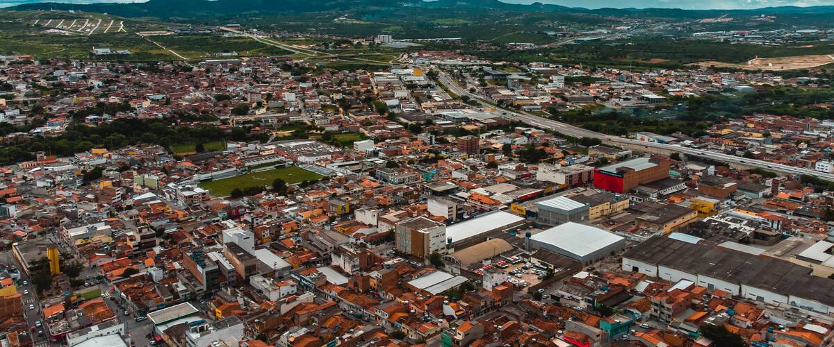 An aerial view of a densely populated city with a mix of residential and commercial buildings, surrounded by mountains and a highway.