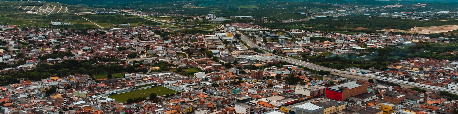 An aerial view of a densely populated city with a mix of residential and commercial buildings, surrounded by mountains and a highway.