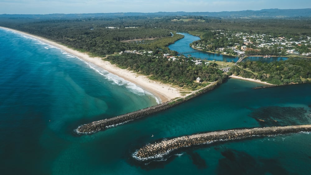 A coastal landscape with a sandy beach, a river, and a rocky breakwater.