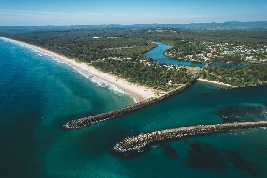 Un paisaje costero con una playa arenosa, un río y un rompeolas rocoso.