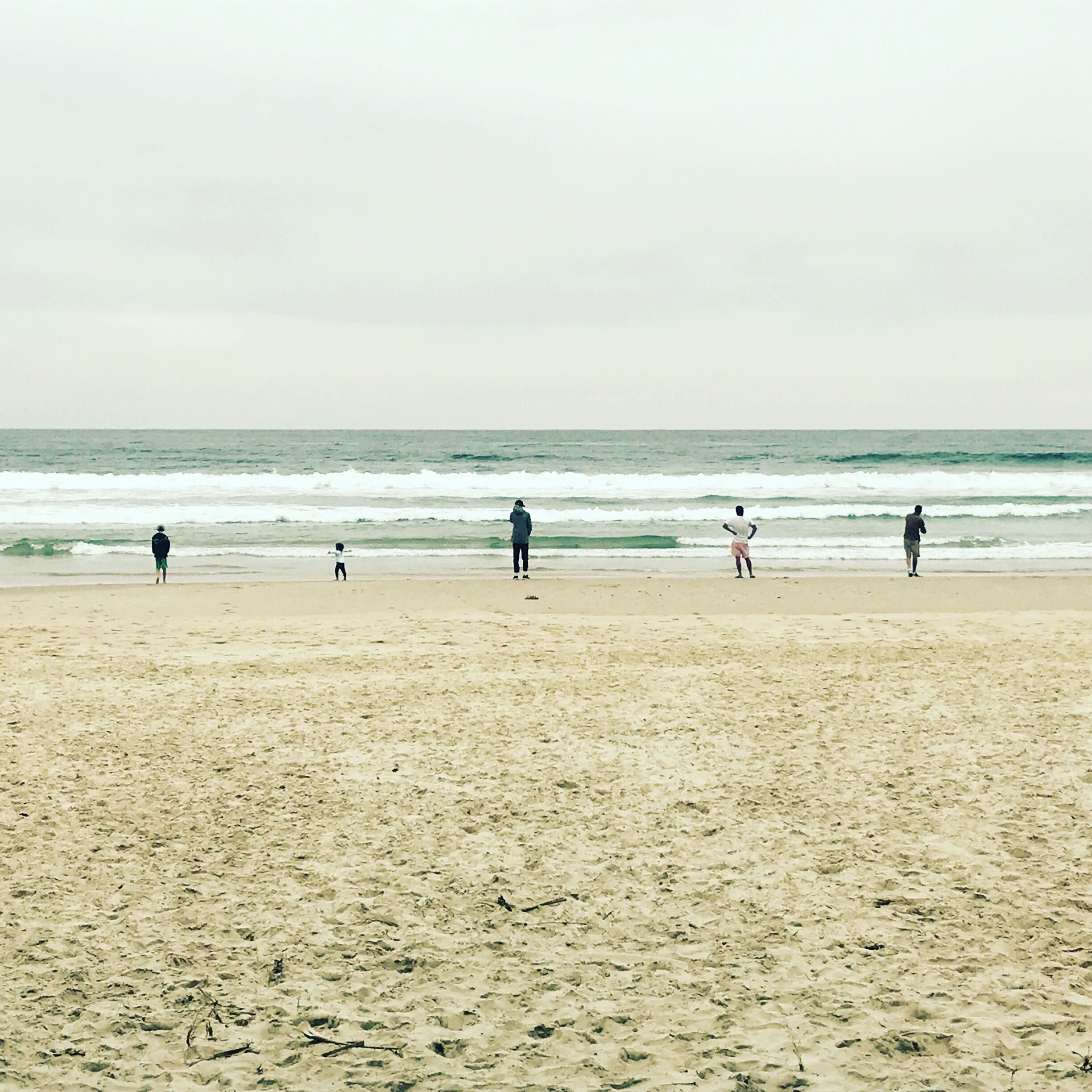 A sandy beach with a calm sea and overcast sky.