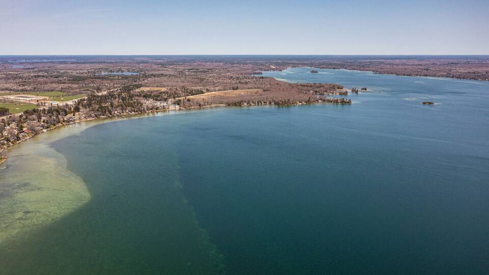 An aerial view of a coastal town with a bay, surrounded by forested areas and a distant cityscape.