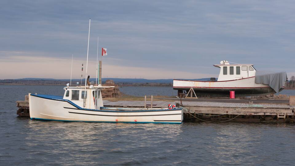 Two boats docked at a pier with a calm lake and distant hills in the background.