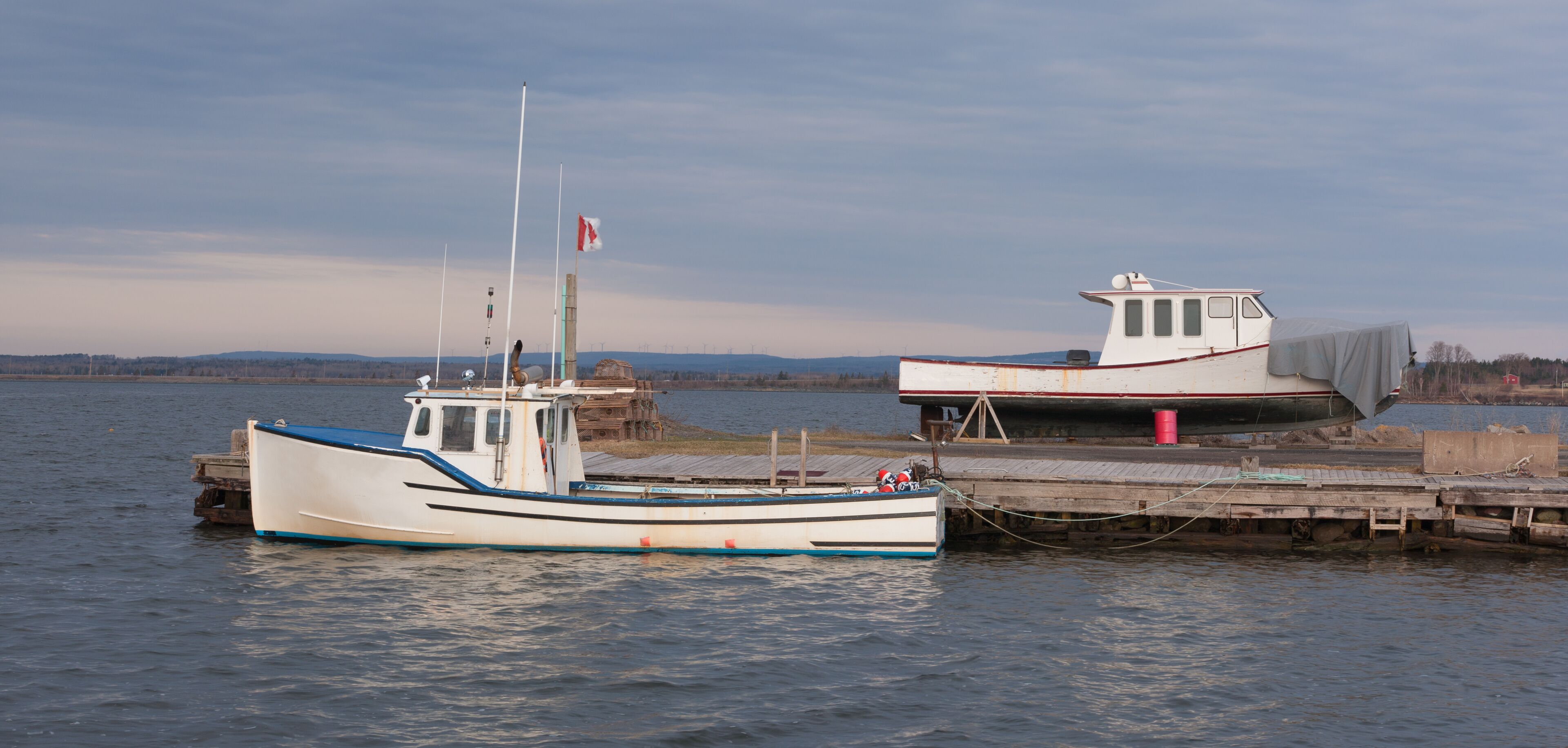 Two boats docked at a pier with a calm lake and distant hills in the background.