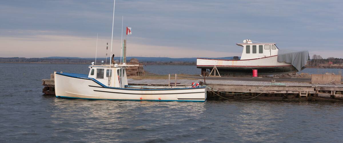 Two boats docked at a pier with a calm lake and distant hills in the background.