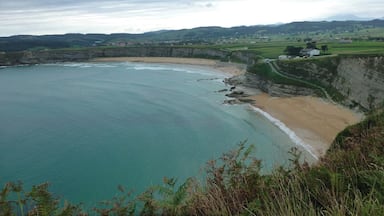 Un paisaje costero con una playa arenosa, acantilados y un pueblo lejano.