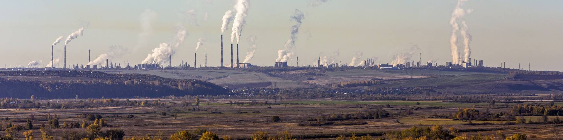 A landscape with multiple industrial chimneys emitting smoke against a clear sky.