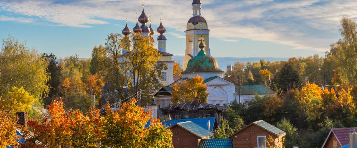 A church with multiple domes and a bell tower, surrounded by autumn-colored trees and residential buildings.