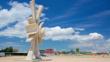 Una gran escultura abstracta en una zona arenosa con edificios al fondo.