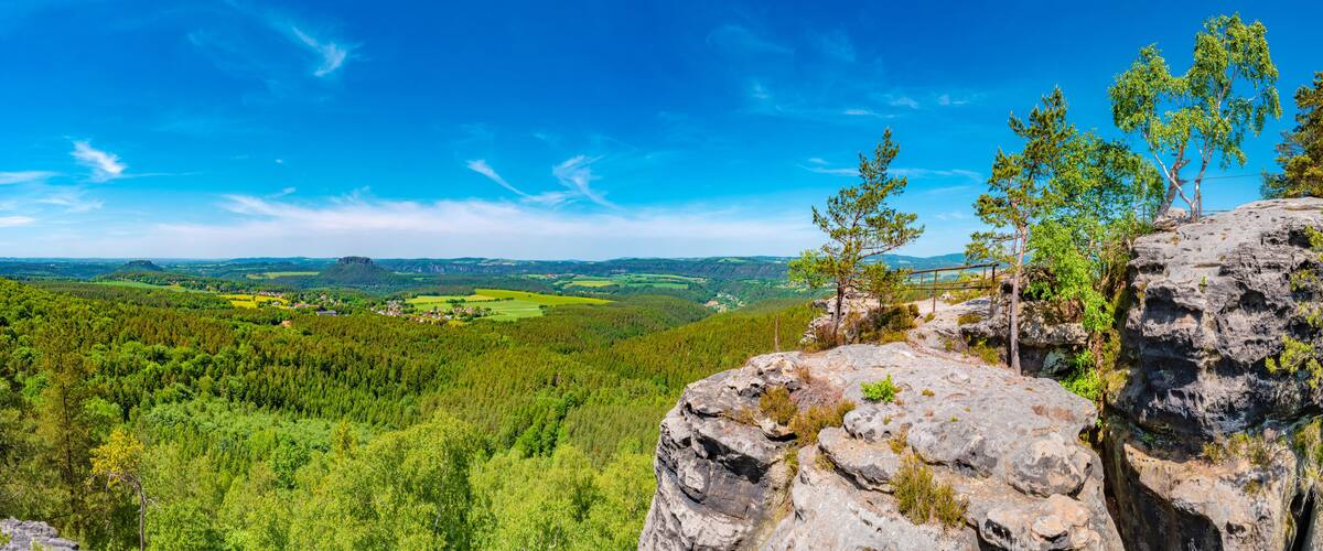 A mountainous landscape with a forested valley, a clear blue sky, and a rocky outcrop in the foreground.