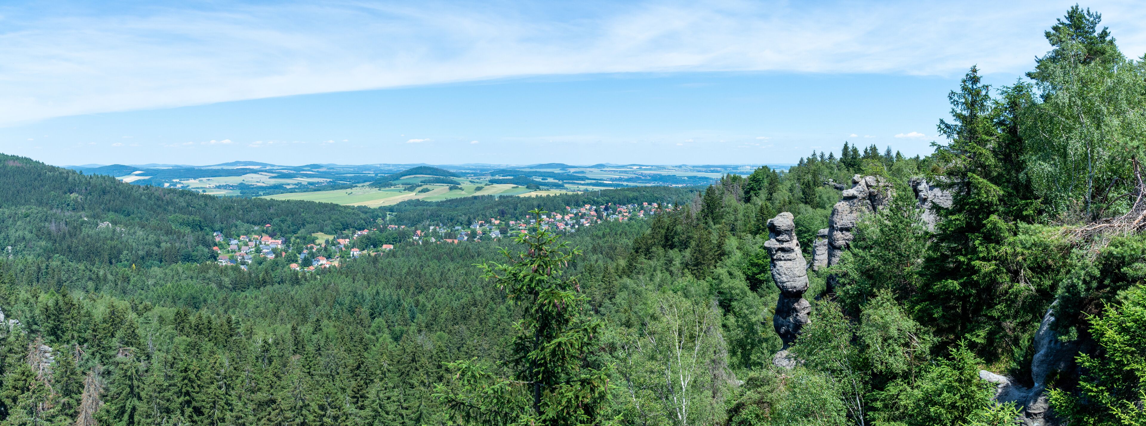 A mountainous landscape with dense forests, a village, and distinctive rock formations.
