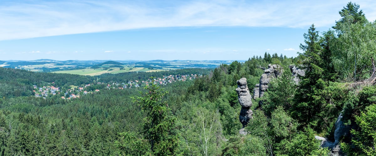 A mountainous landscape with dense forests, a village, and distinctive rock formations.