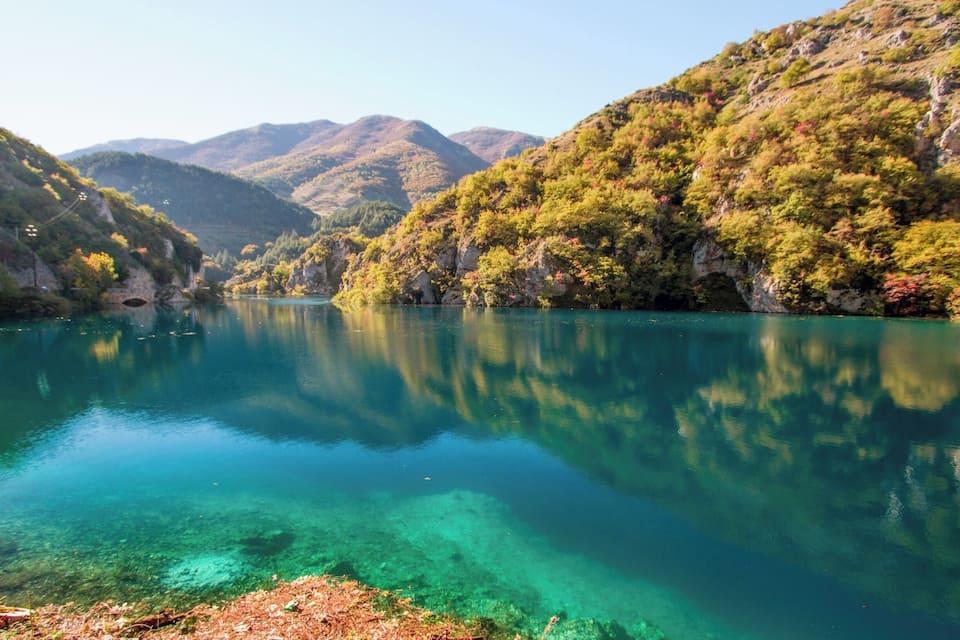 A clear lake surrounded by hills with dense green foliage.