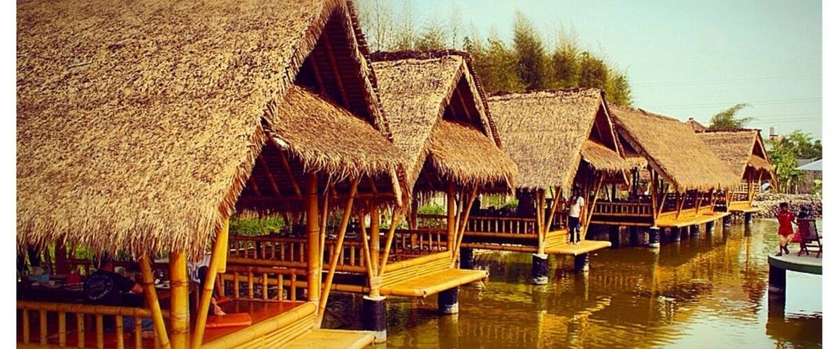 Overwater bungalows with thatched roofs on stilts over calm water.