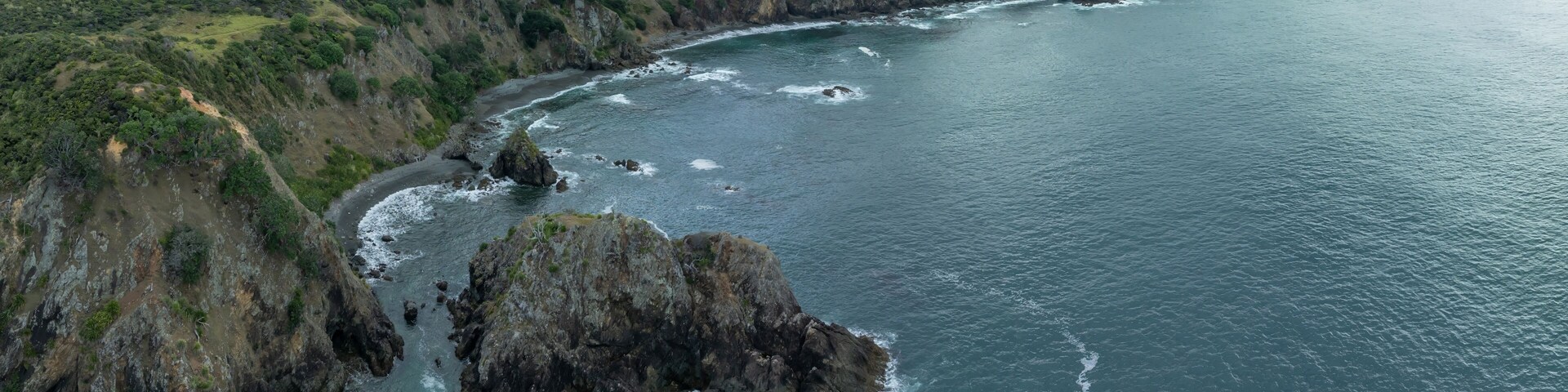 A coastal landscape with rocky cliffs, a bay, and distant mountains.