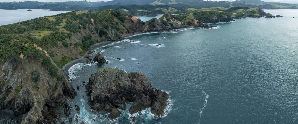 A coastal landscape with rocky cliffs, a bay, and distant mountains.