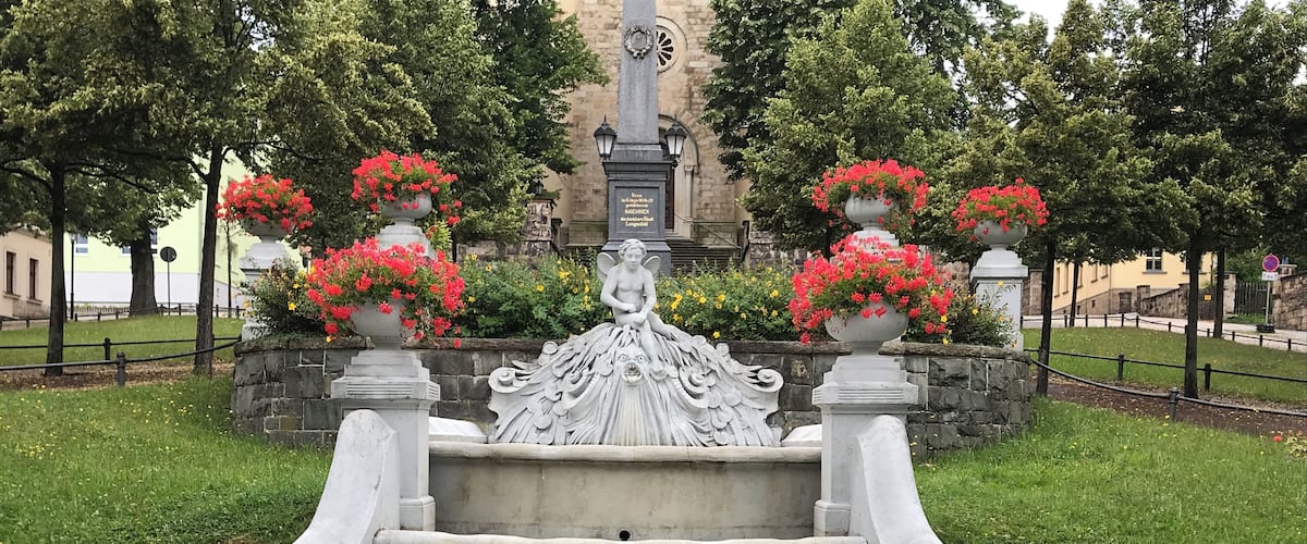 A fountain with a statue in the center, surrounded by red flowers and greenery.