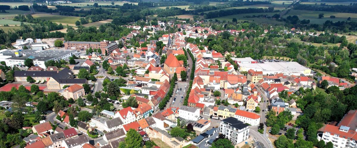 An aerial view of a town with a prominent church, surrounded by residential buildings and green fields.
