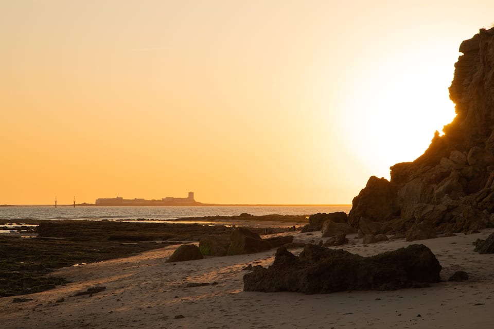 A coastal sunset with rocky cliffs and a distant cityscape.