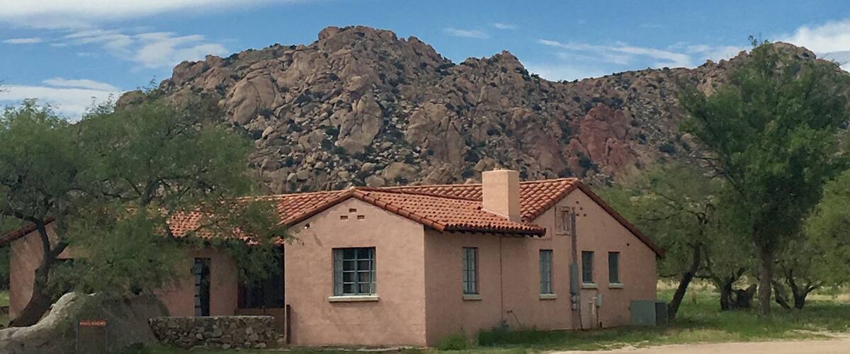 A house with a red-tiled roof, surrounded by trees and a rocky mountain in the background.